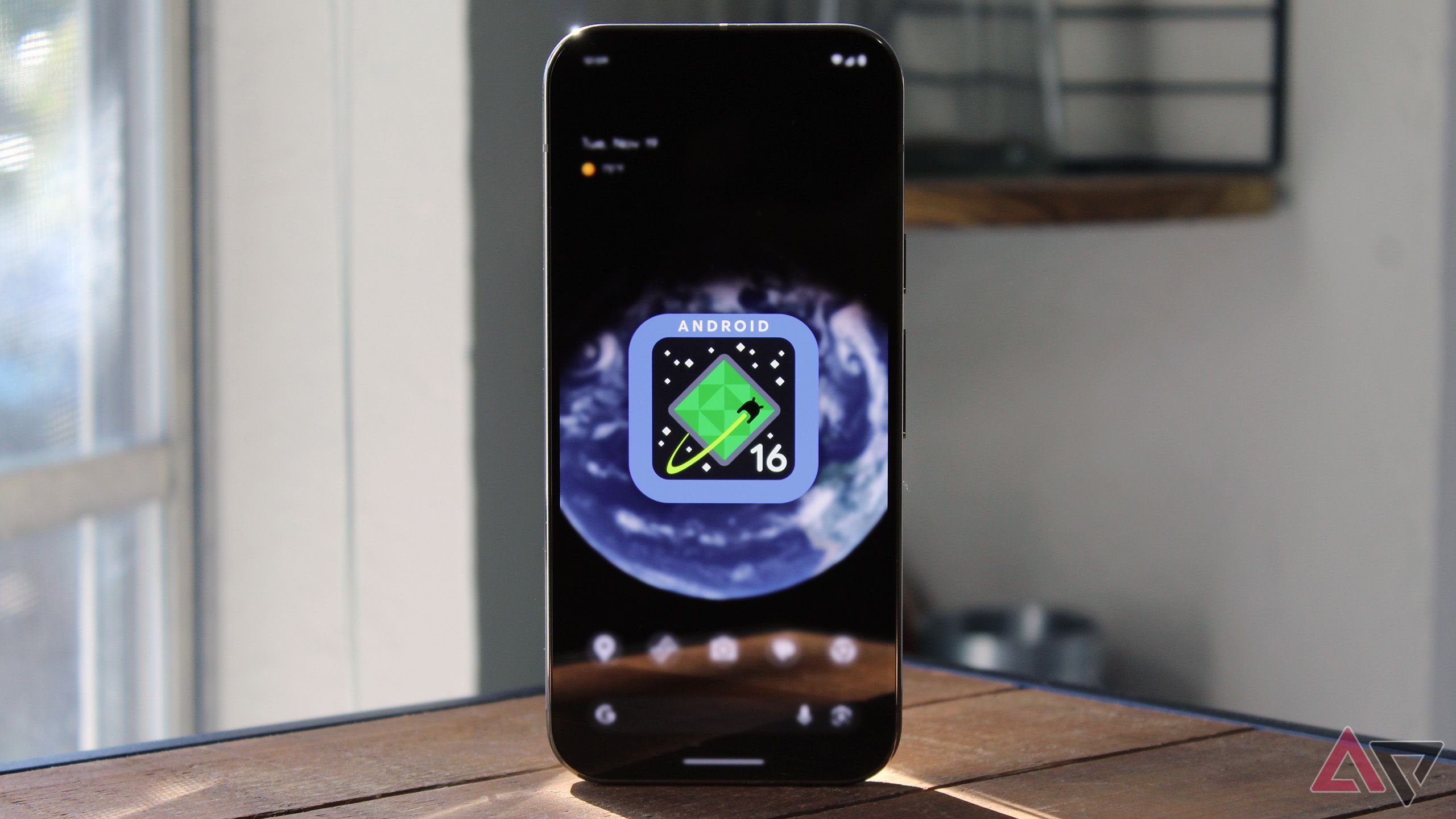 A google Pixel with the Android 16 logo sits stands on a table 