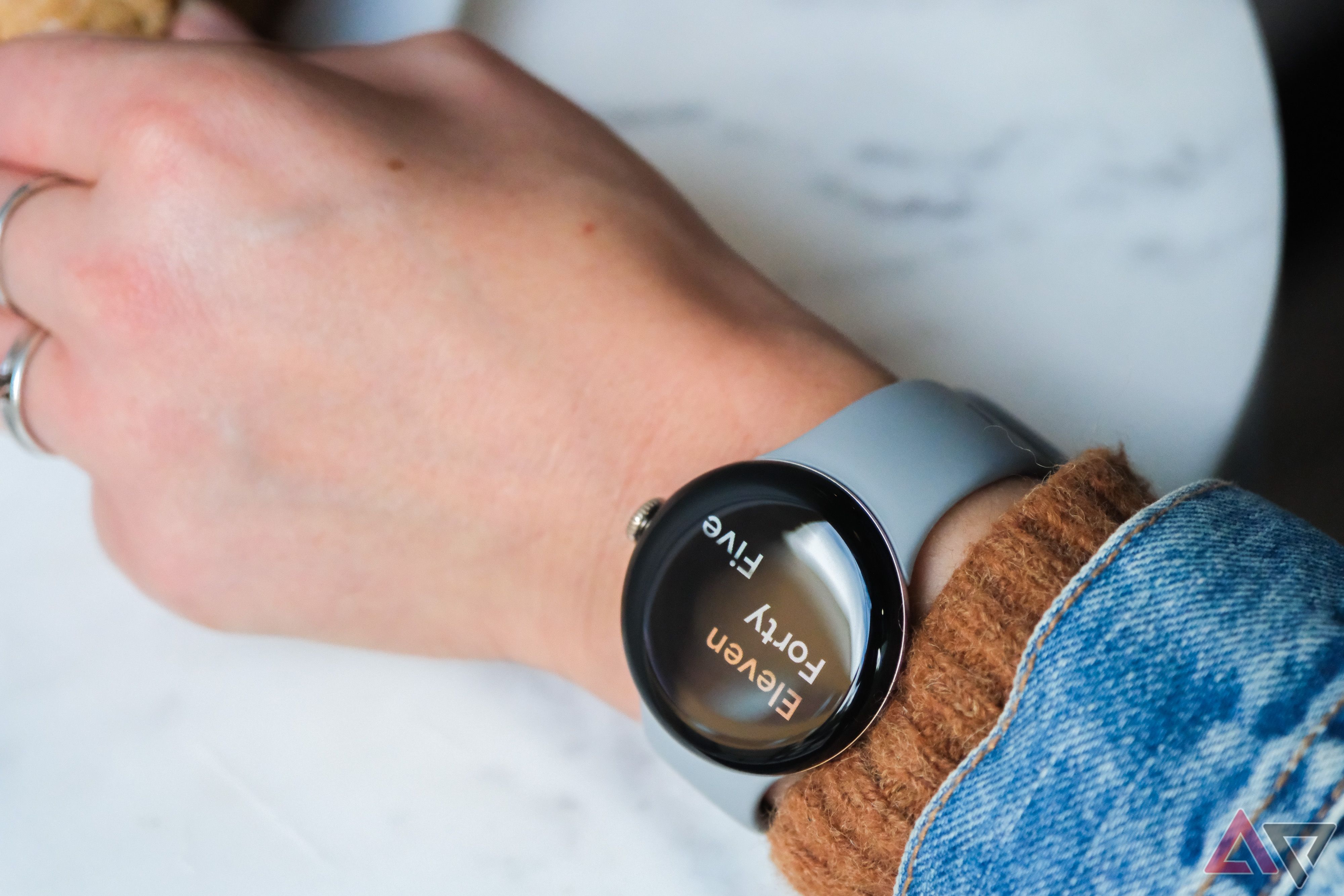A person wearing a jacket and sweater wears a Google Pixel Watch 2 with the time on the AOD