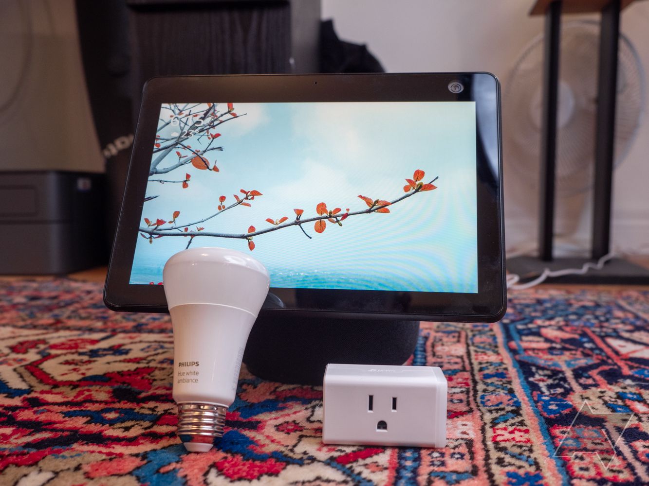 A smart display, smart lightbulb, and smart power plug on a multi-color carpet