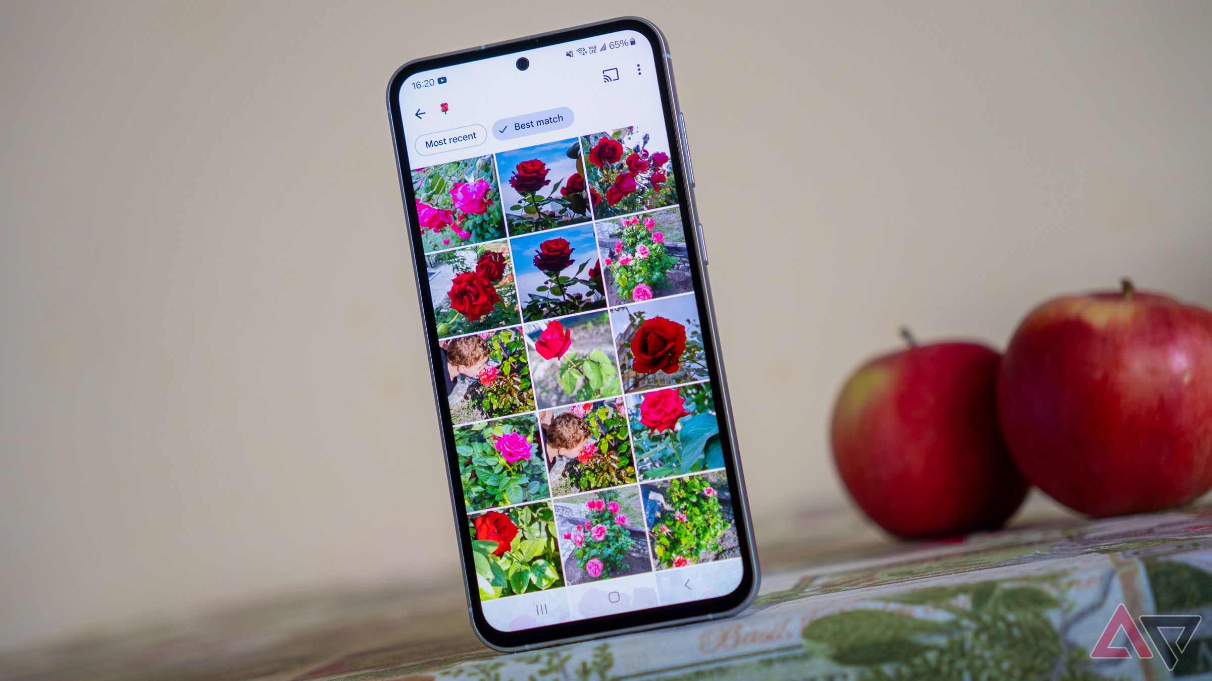 a phone displaying google photos search results on a table next to two red apples