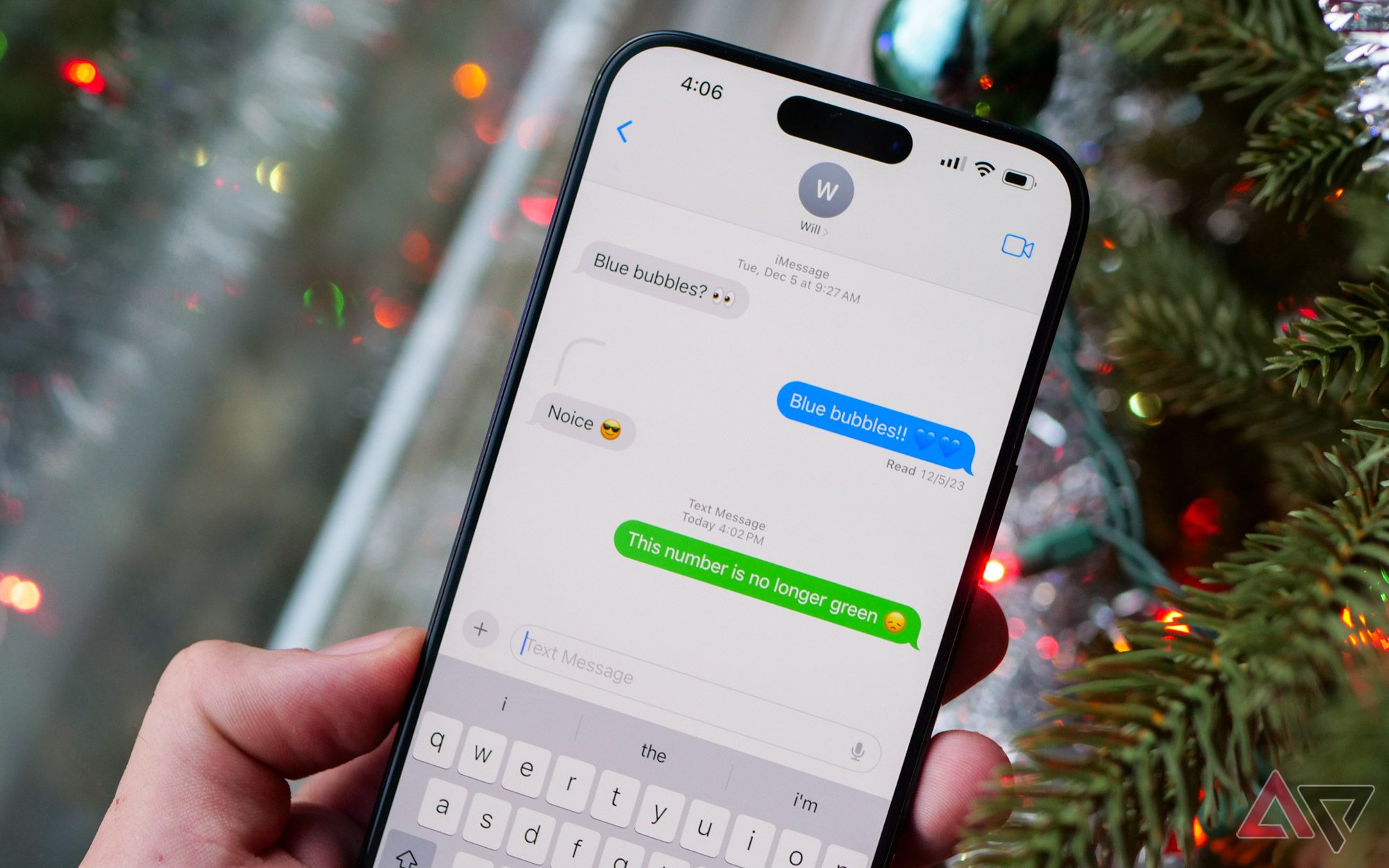An iPhone 15 Pro Max held in front of a Christmas tree with Messages open.