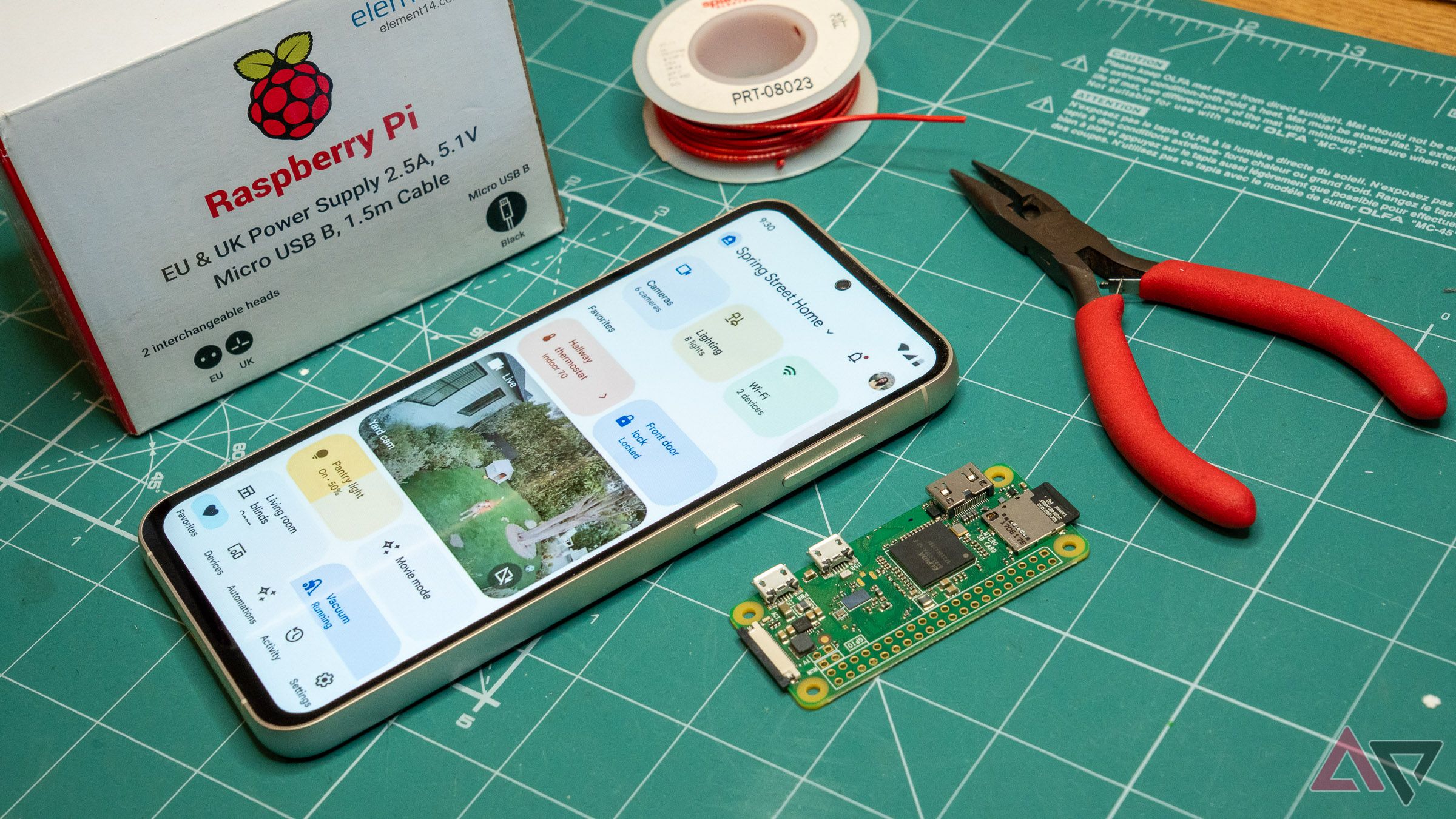 a phone displaying the google home app on a green mat next to pliers, wire, a raspberry pi, and a white box