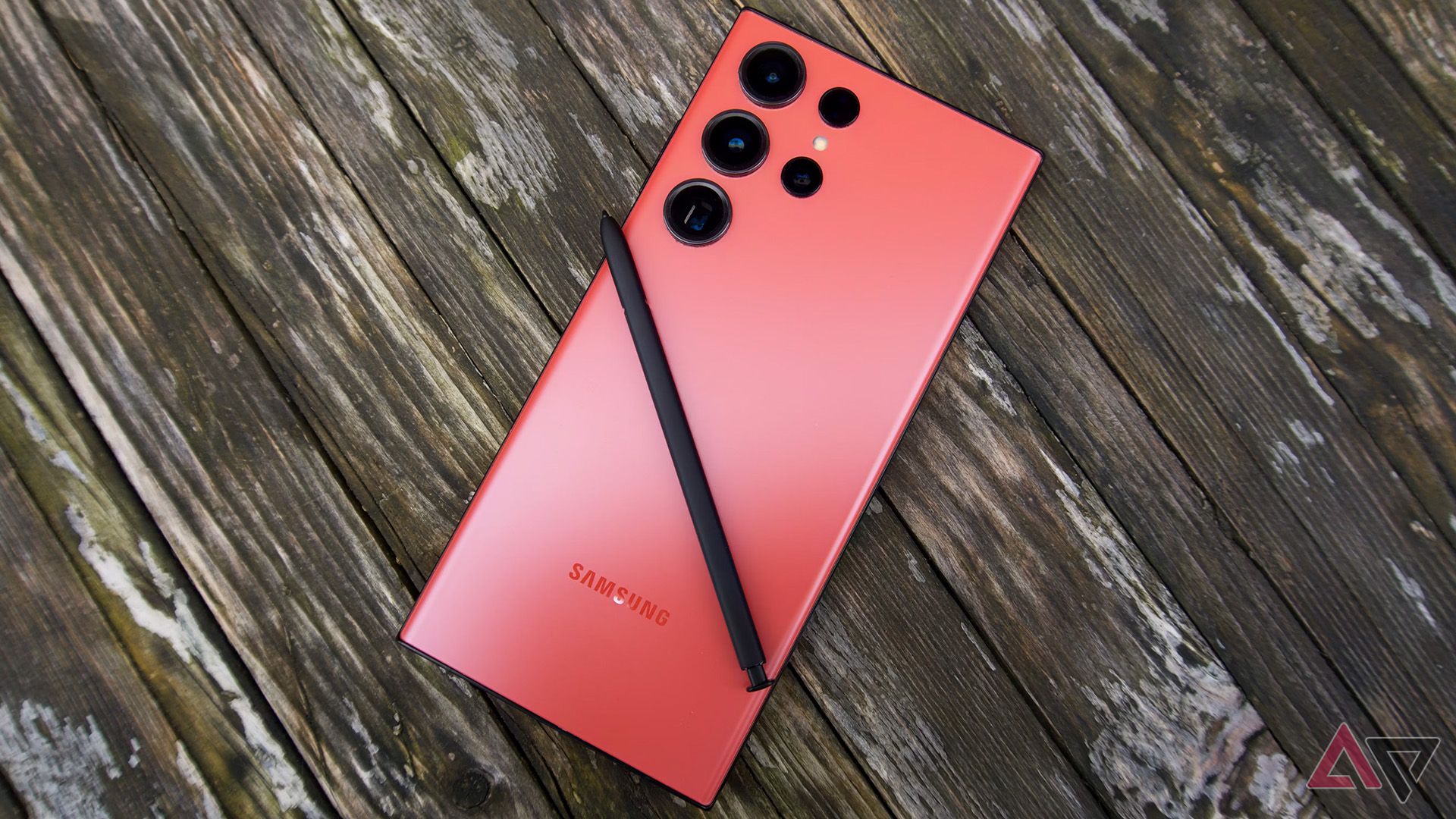A photo of a red Galaxy S23 Ultra face down on a wooden surface with the S Pen sat on top.