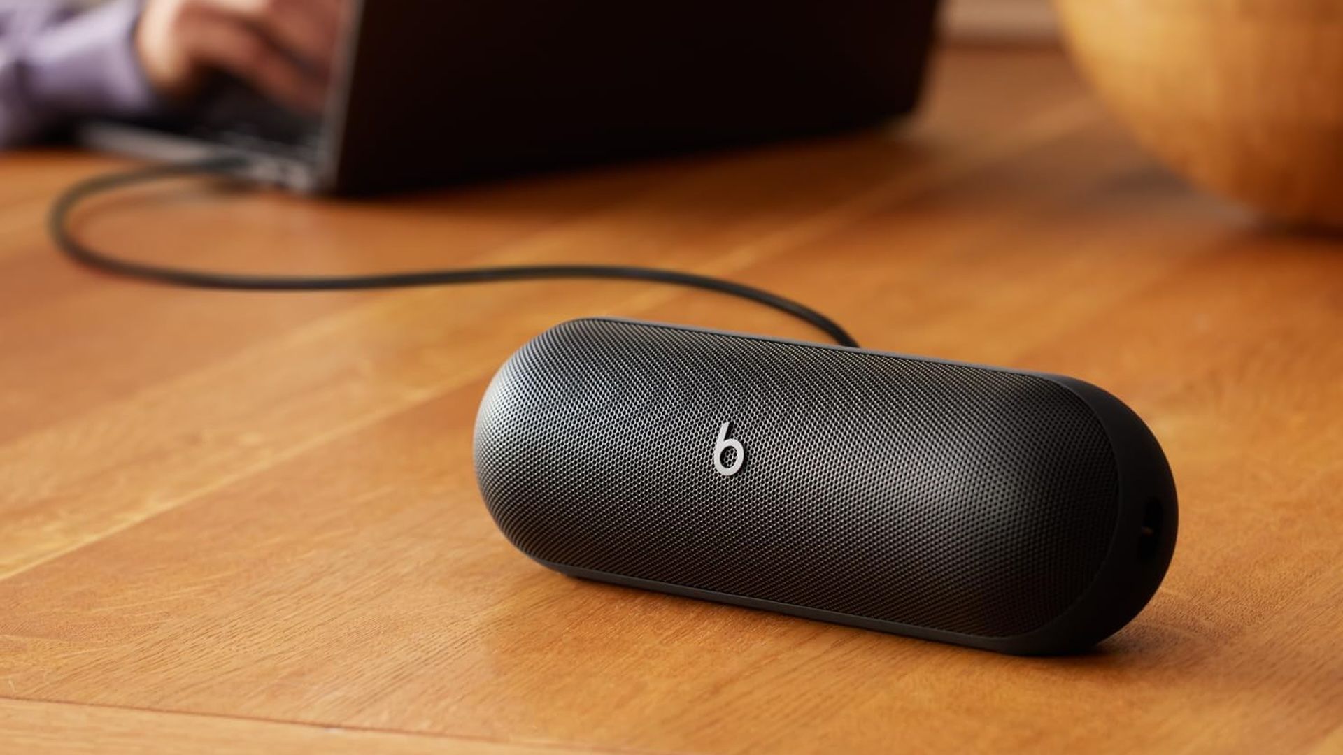 A black Beats Pill in the foreground with a laptop in the background.