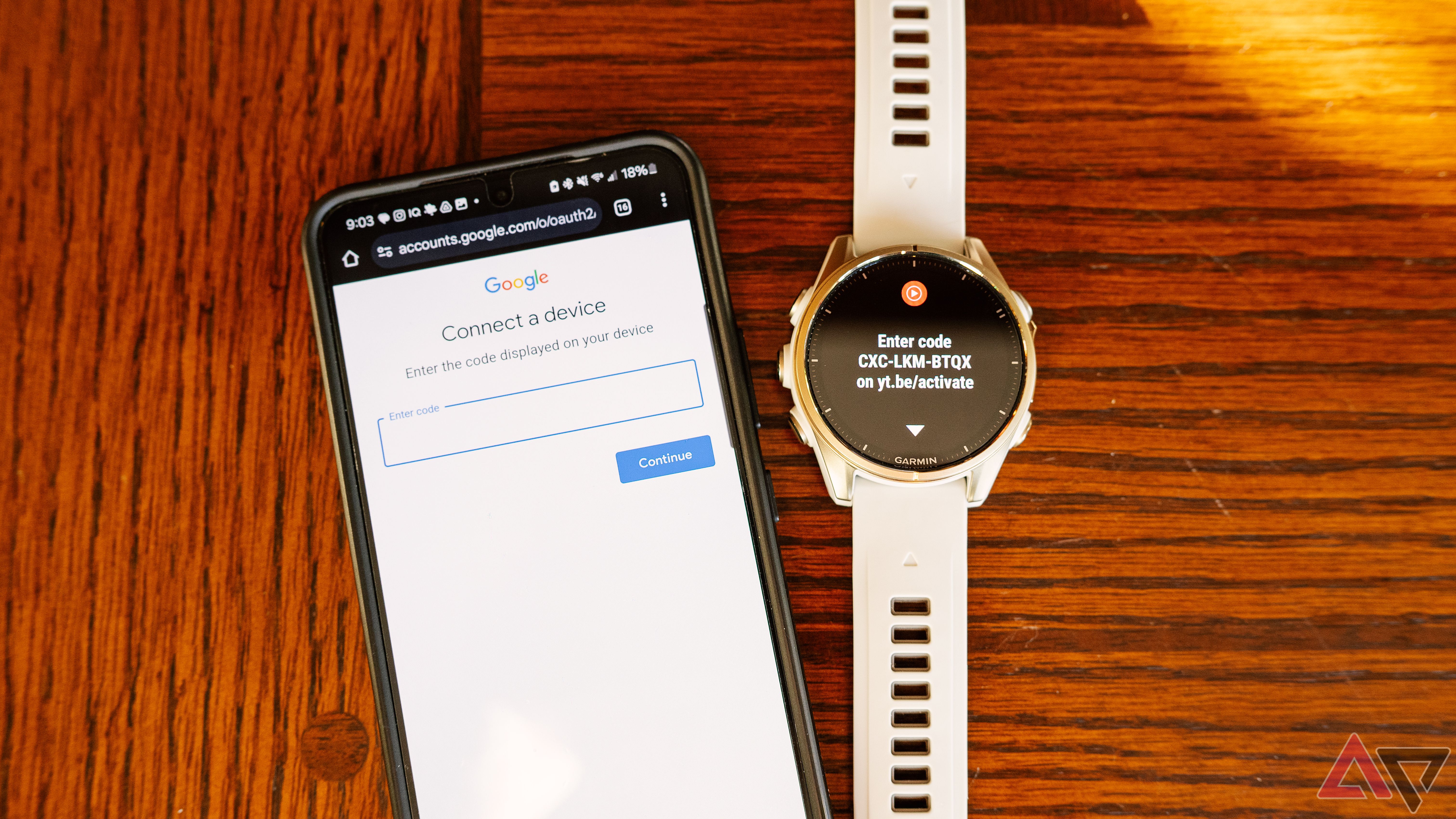 A Samsung Galaxy phone sits next to a Garmin fenix 8 on a wood table. 