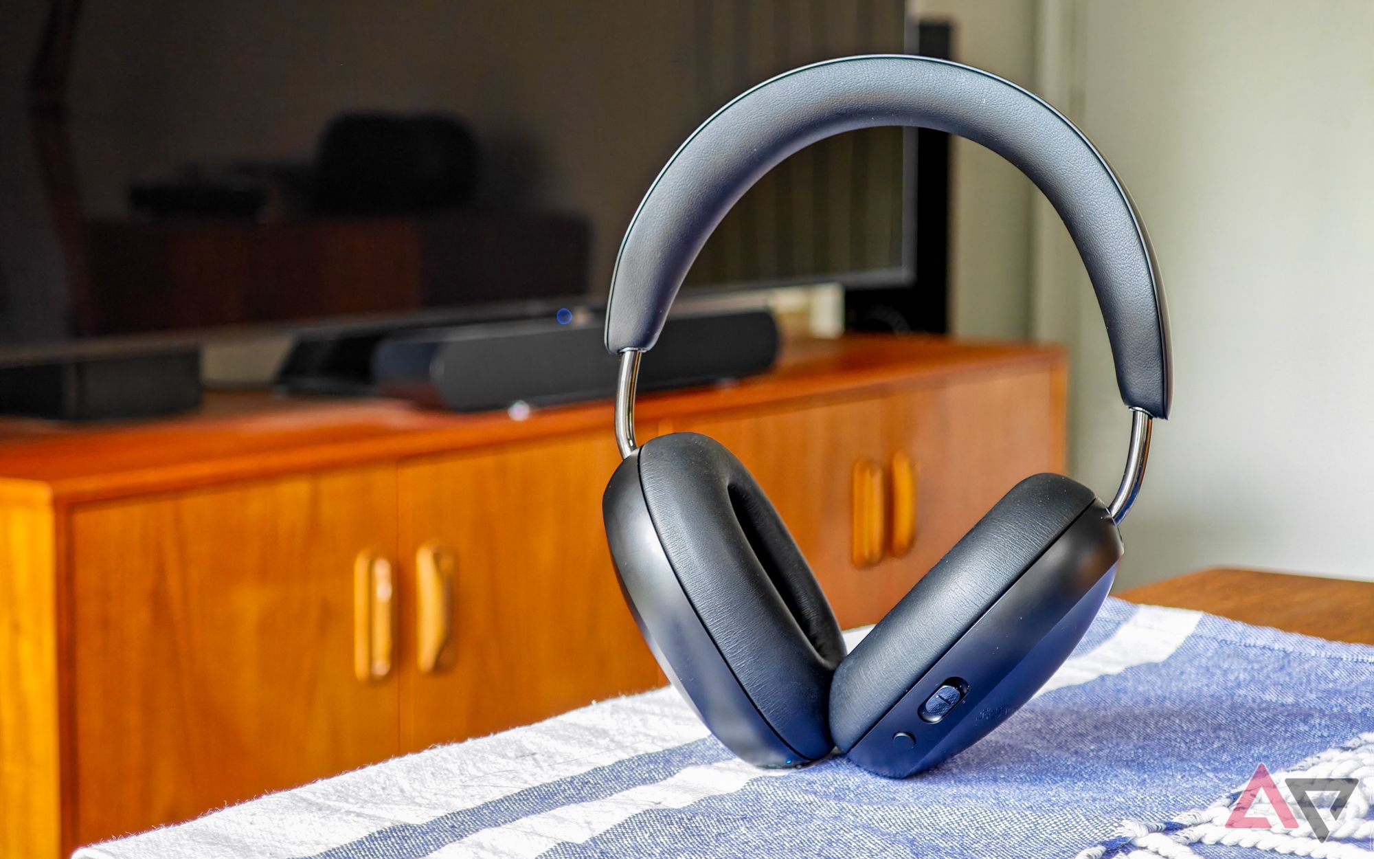 Black Sonos Ace headphones standing upright on a table with a TV in the background