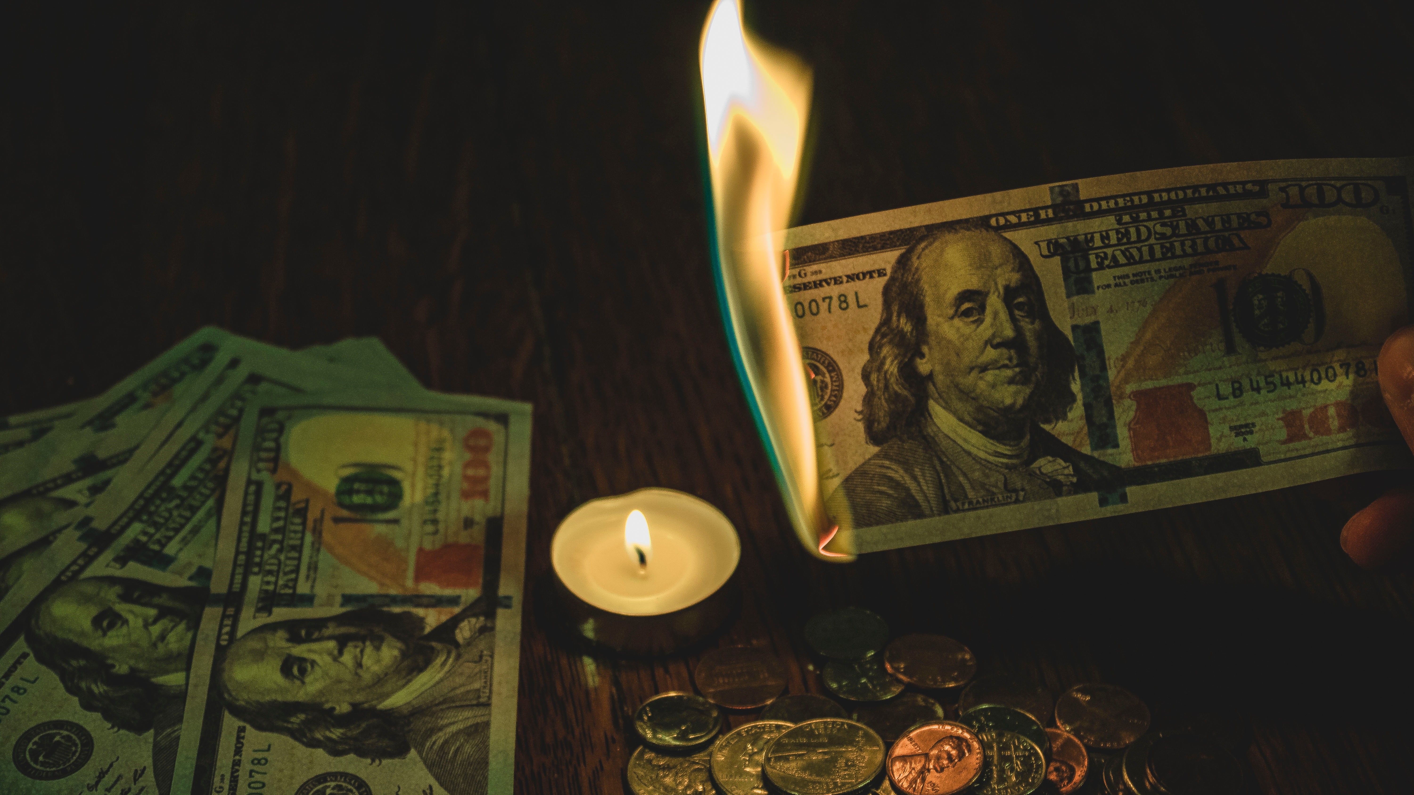 Paper money held over candle flame, alight in fire.
